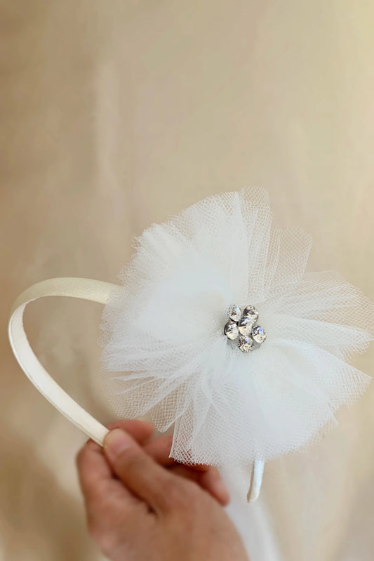 White tulle flower motif headband with a decorative crystal on a beige background