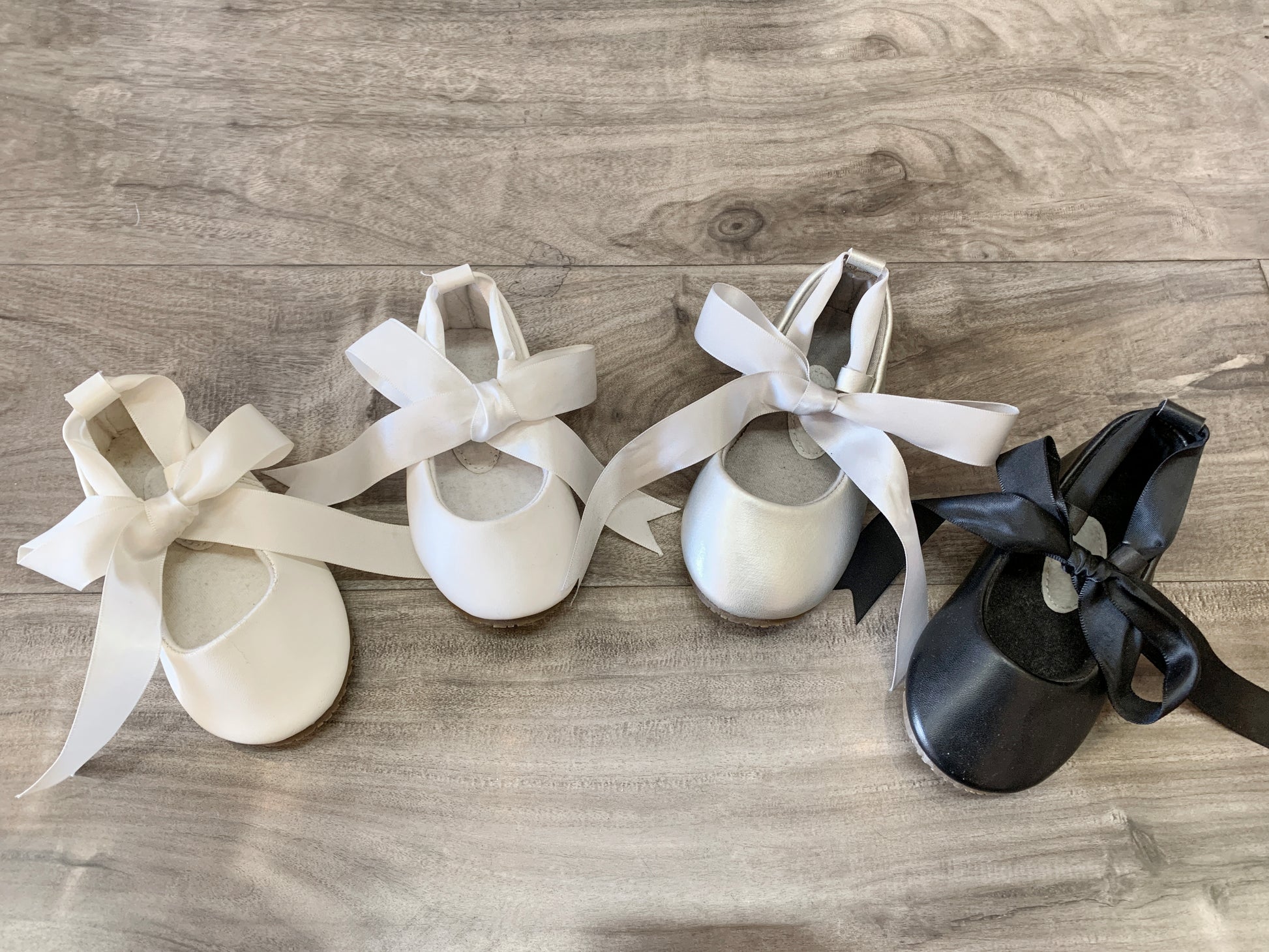 Three pairs of ballet shoes with ribbons on a wooden floor.
