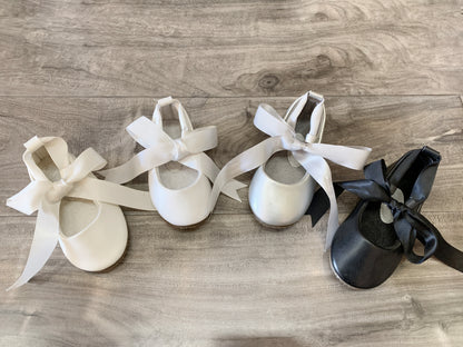 Three pairs of ballet shoes with ribbons on a wooden floor.