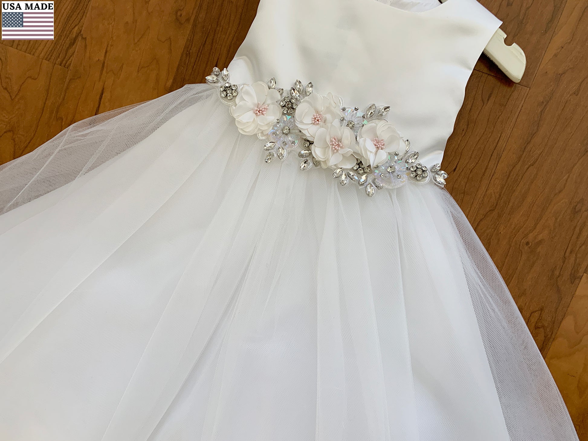 White flower girl dress with floral embellishments on a wooden background