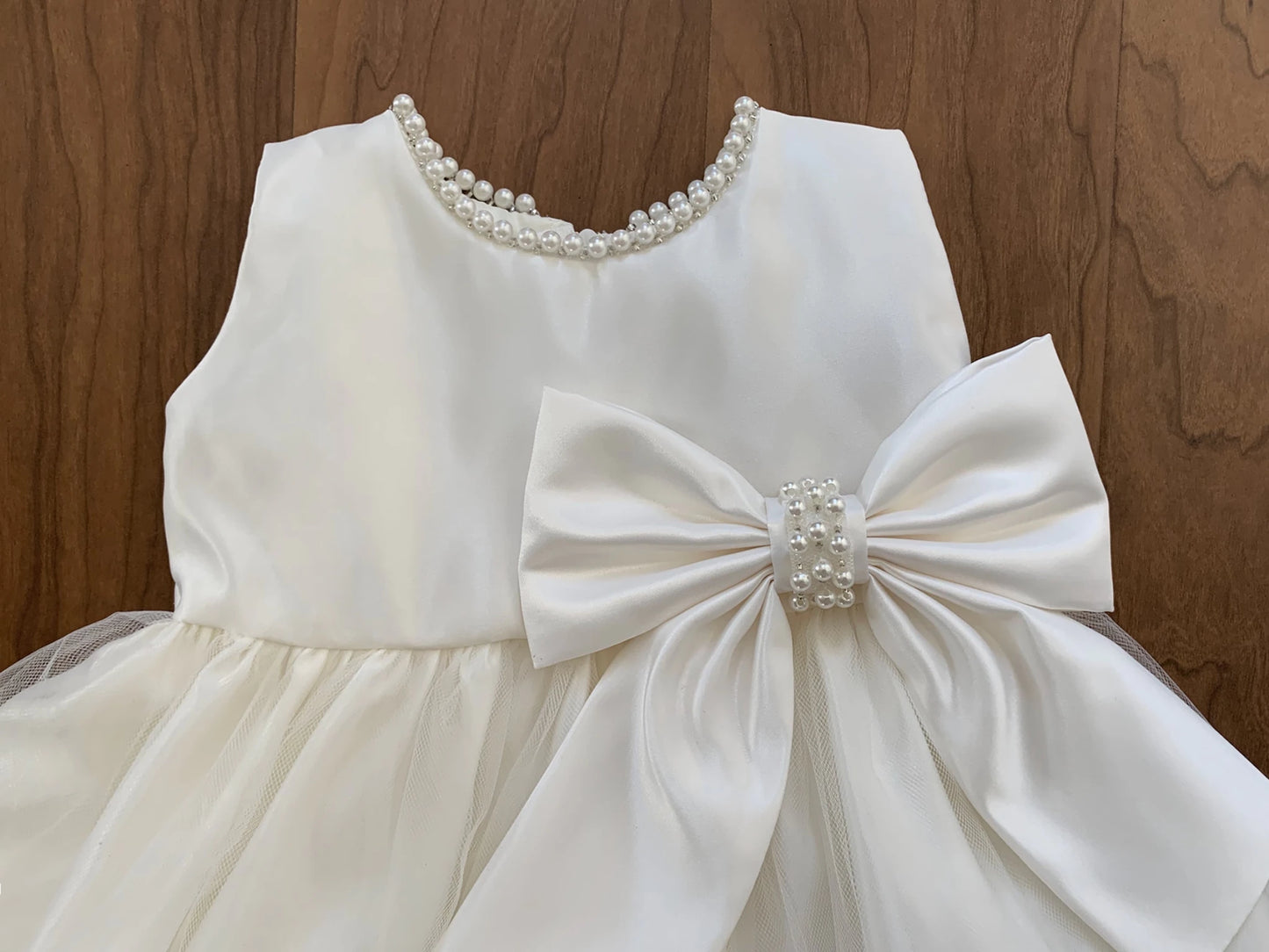 Ivory dress with a large bow and pearl details on a wooden background