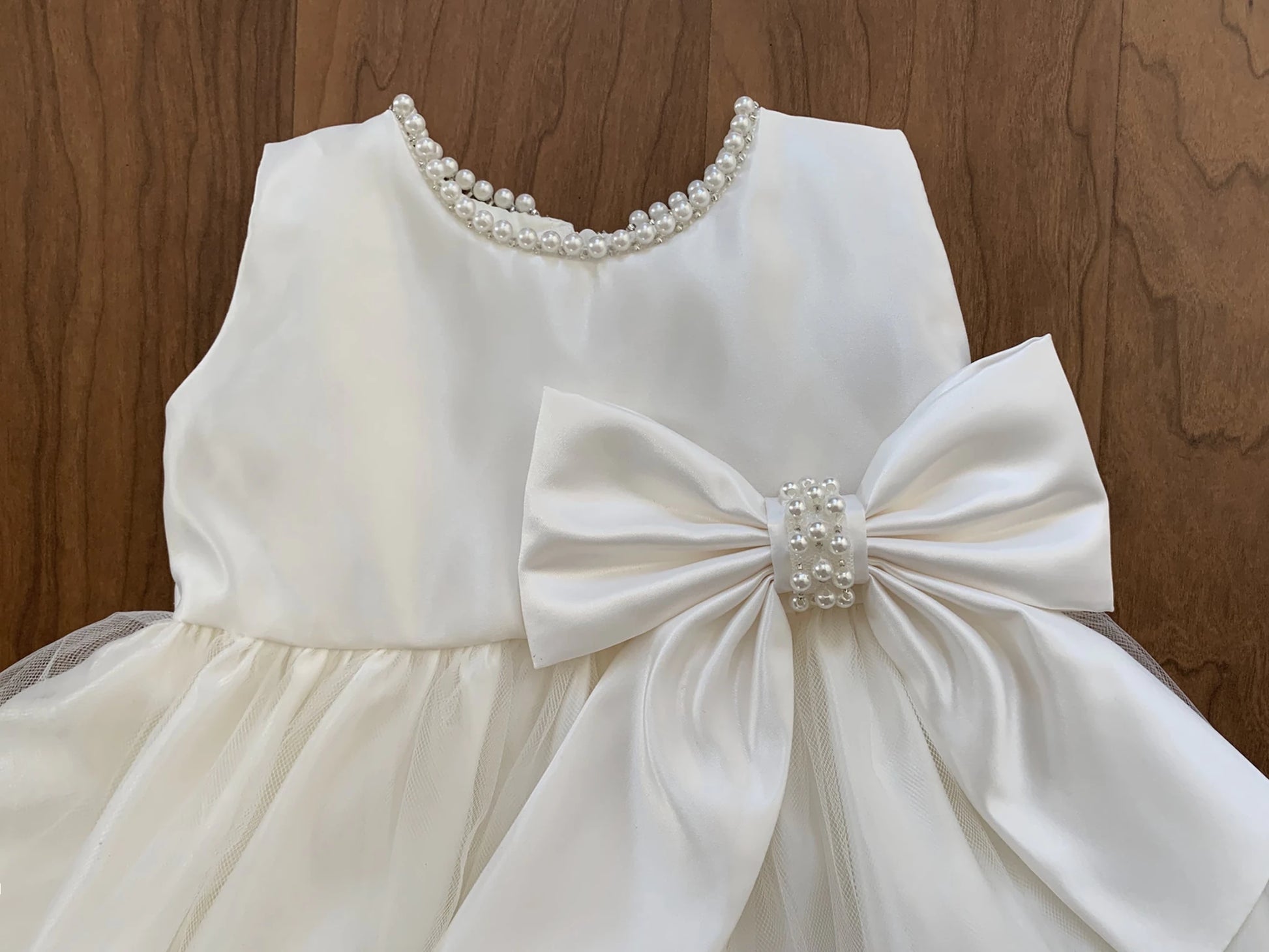 Ivory dress with a large bow and pearl details on a wooden background