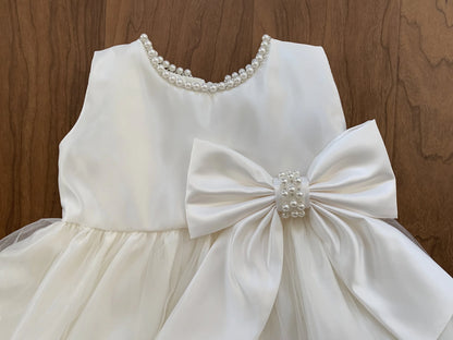 Ivory dress with a large bow and pearl details on a wooden background