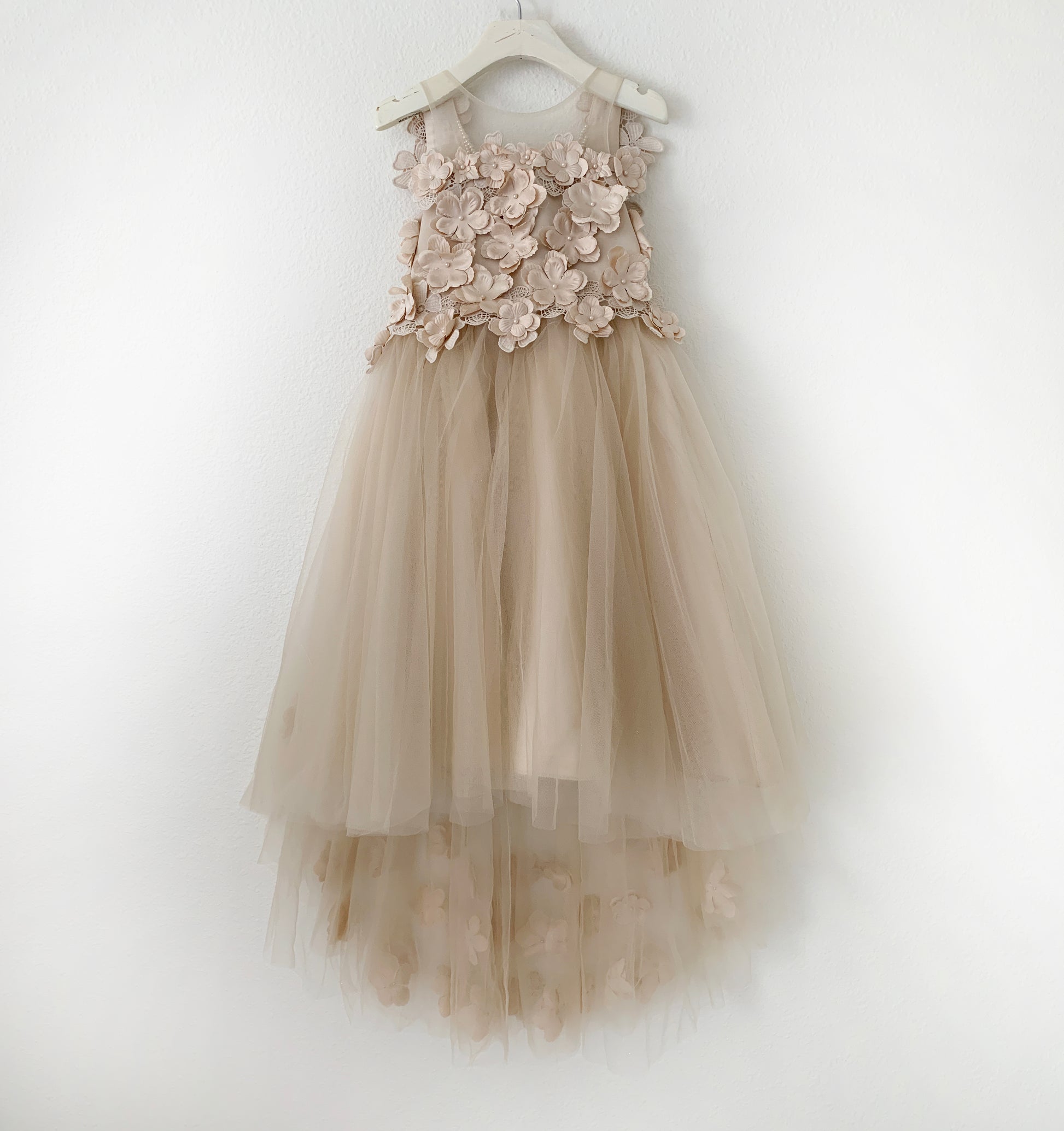Beige flower girl dress with floral details on a white hanger against a white background