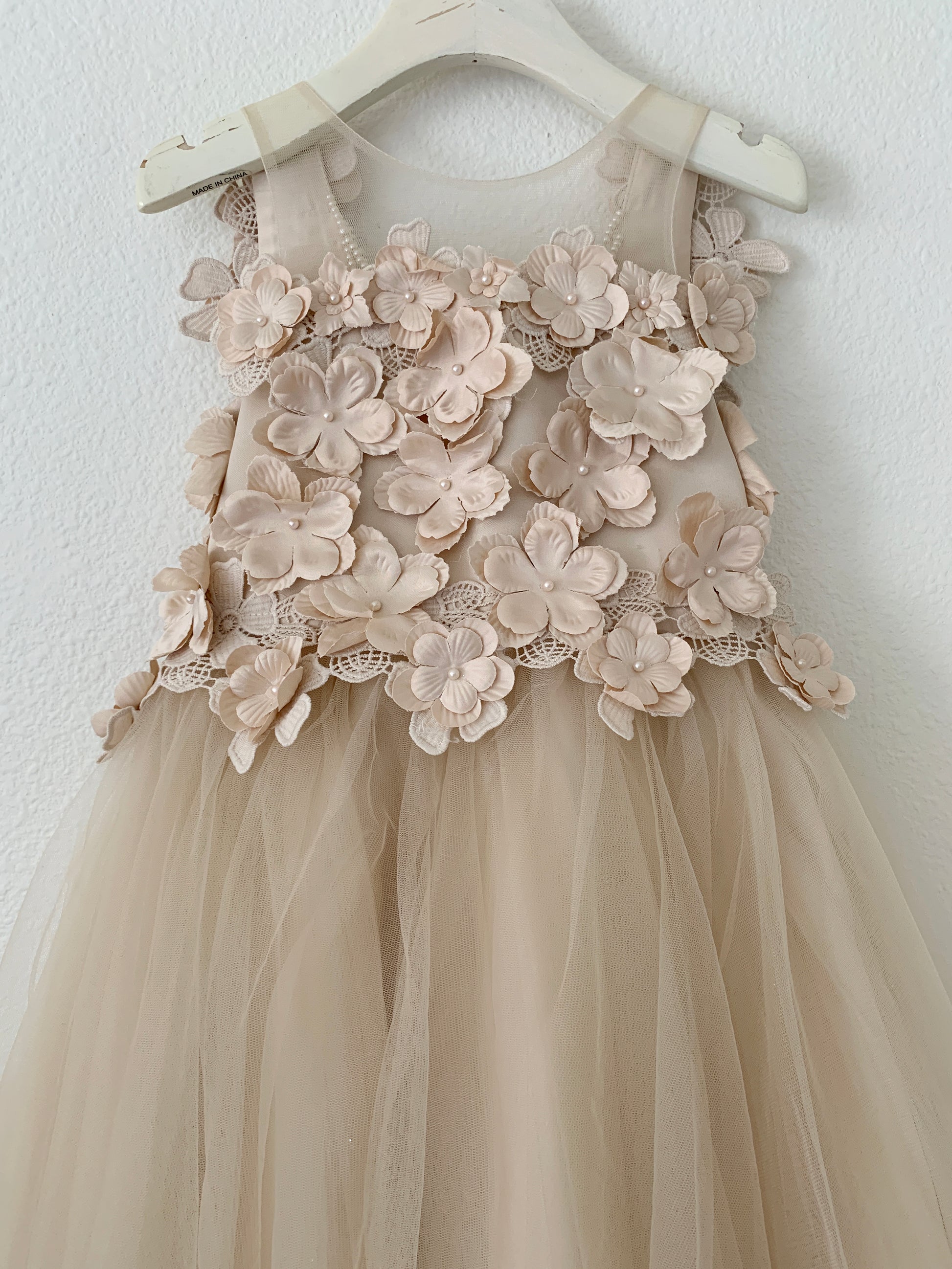 Beige flower girl dress with floral lace details on a white hanger against a white background
