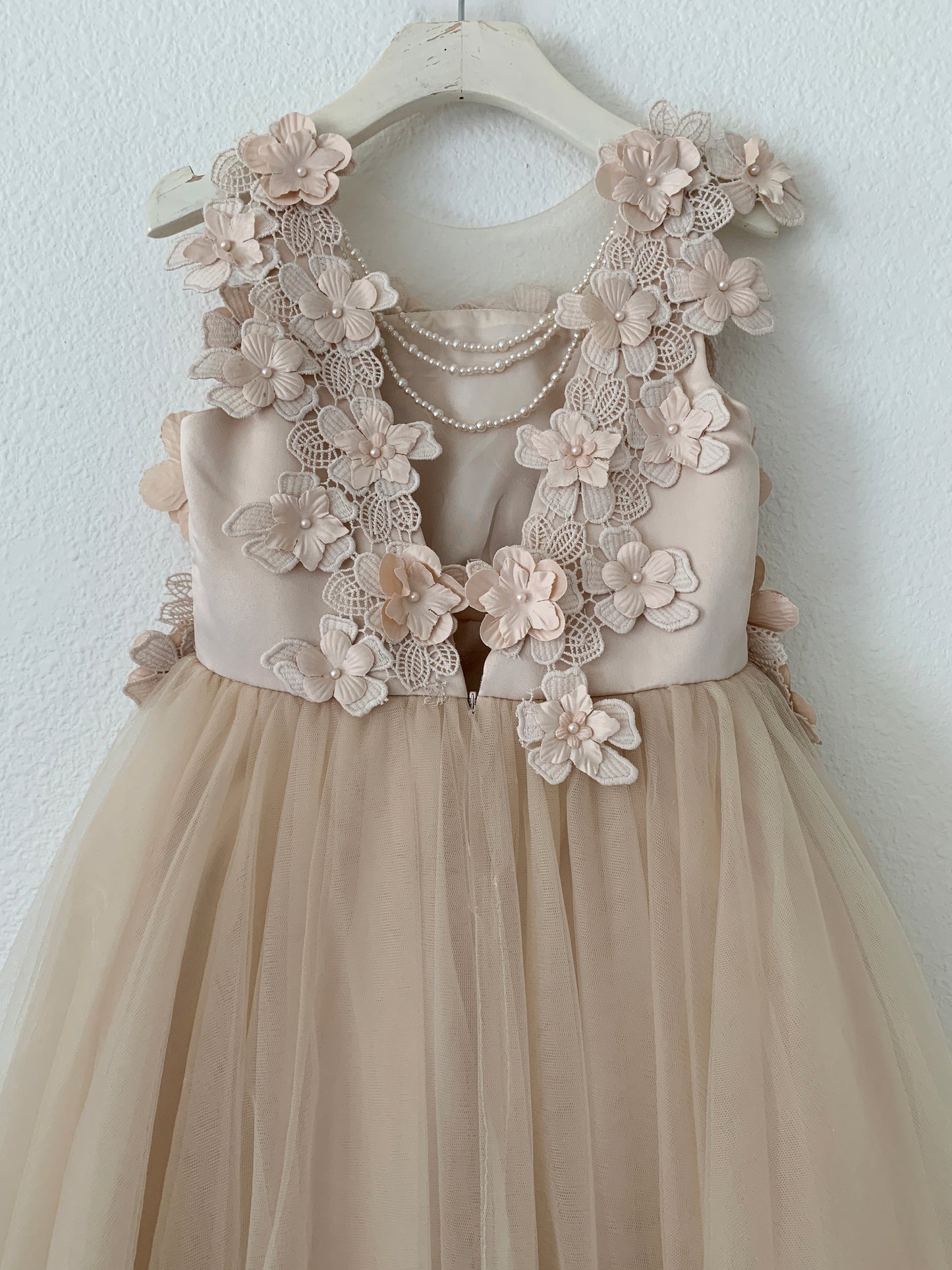 Champagne High-Low Tulle Dress with 3D Flower Lace Top Accentuated with Pearl Trim Flower Girl Dress | Flower Girl Dress - zoomed in view of back of dress on a hanger