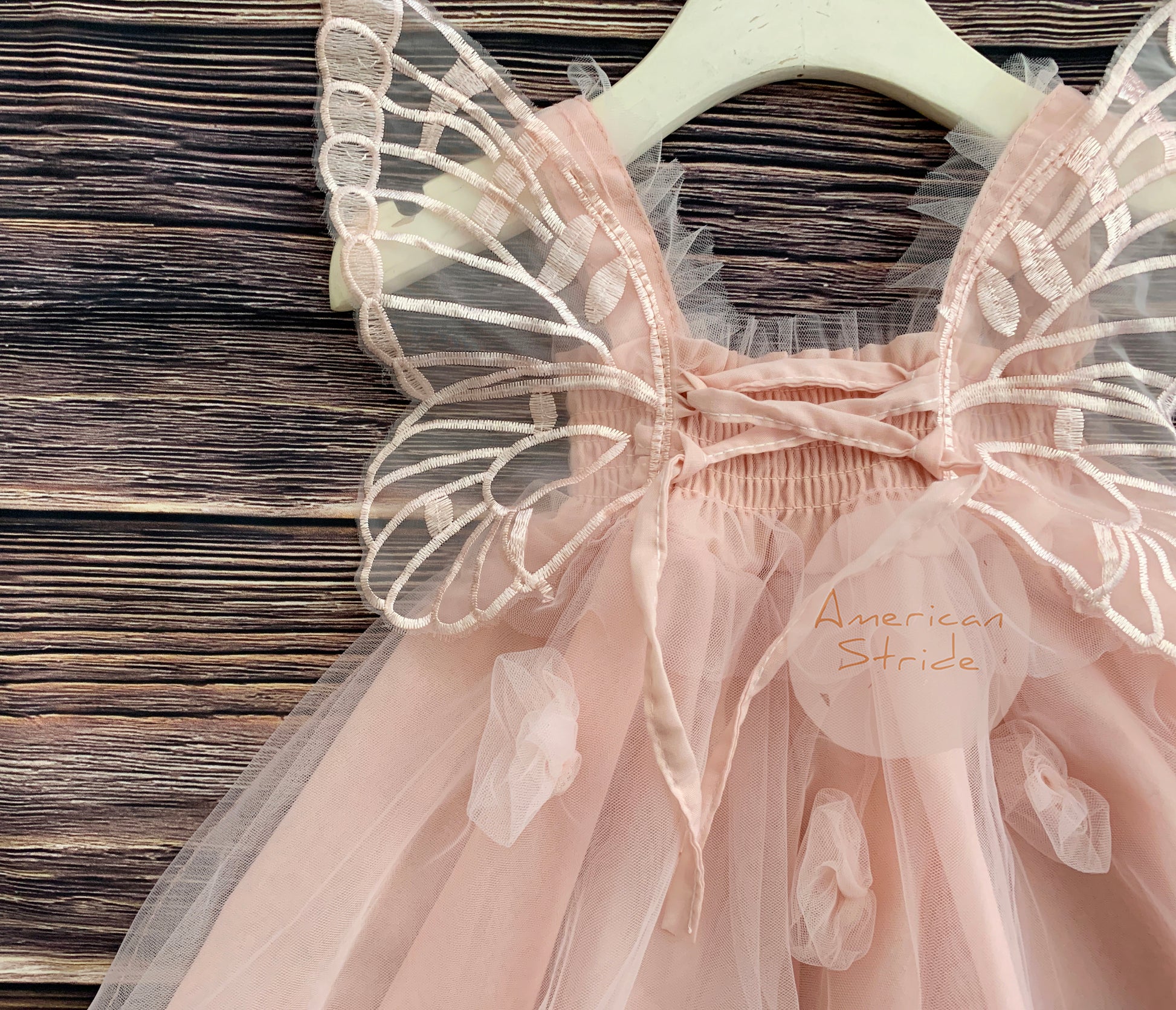 Pink fairy dress with butterfly wings on a wooden surface, brand 'American Stride' visible.