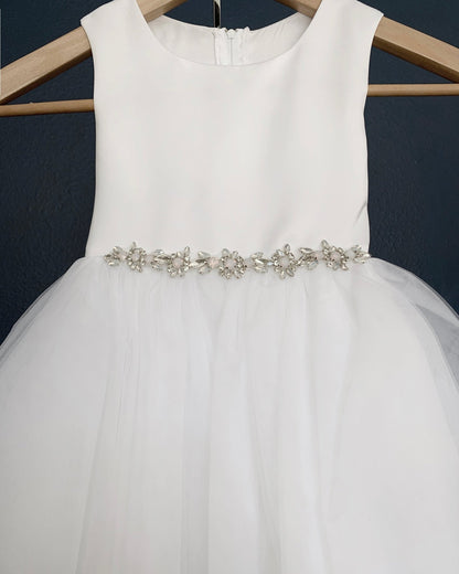 White dress with a decorative belt on a hanger against a dark background