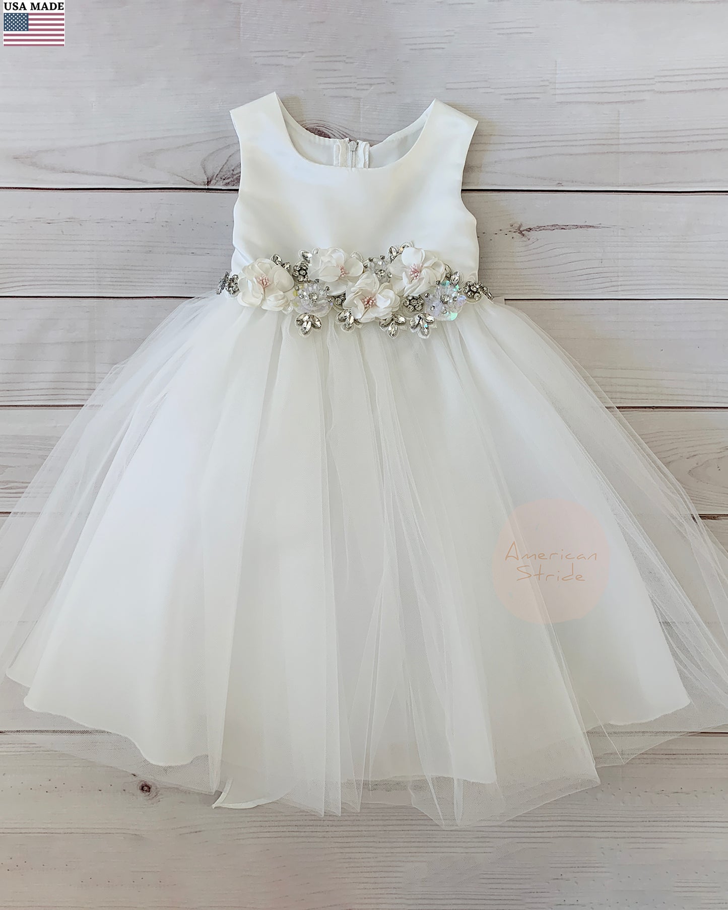 White flower girl dress with floral sash on a wooden background