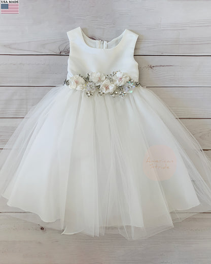 White flower girl dress with floral sash on a wooden background