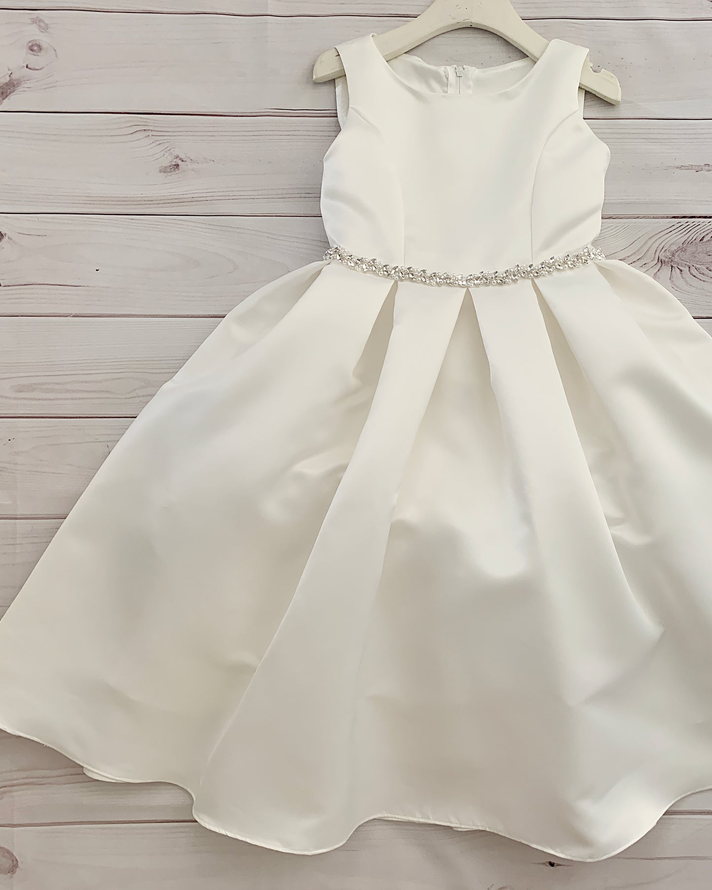 White satin dress with a beaded waistband on a wooden surface