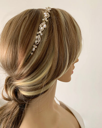 Mannequin head with blonde hair wearing a decorative gold pearl with rhinestones headband against a plain background