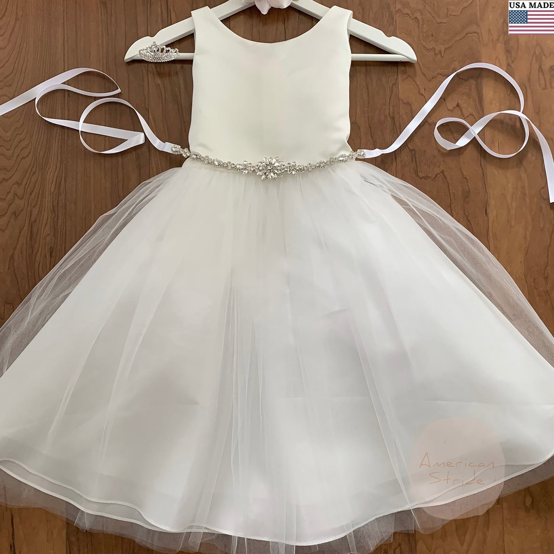 White flower girl dress with a rhinestone flower motif belt on a wooden background