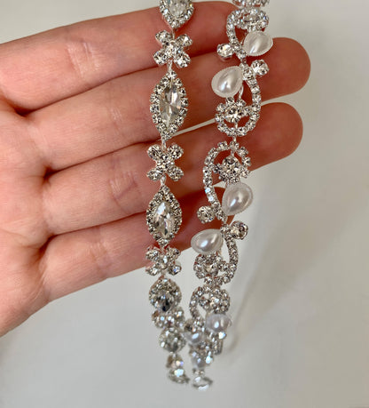 Silver jewelry piece held by a hand on a plain background
