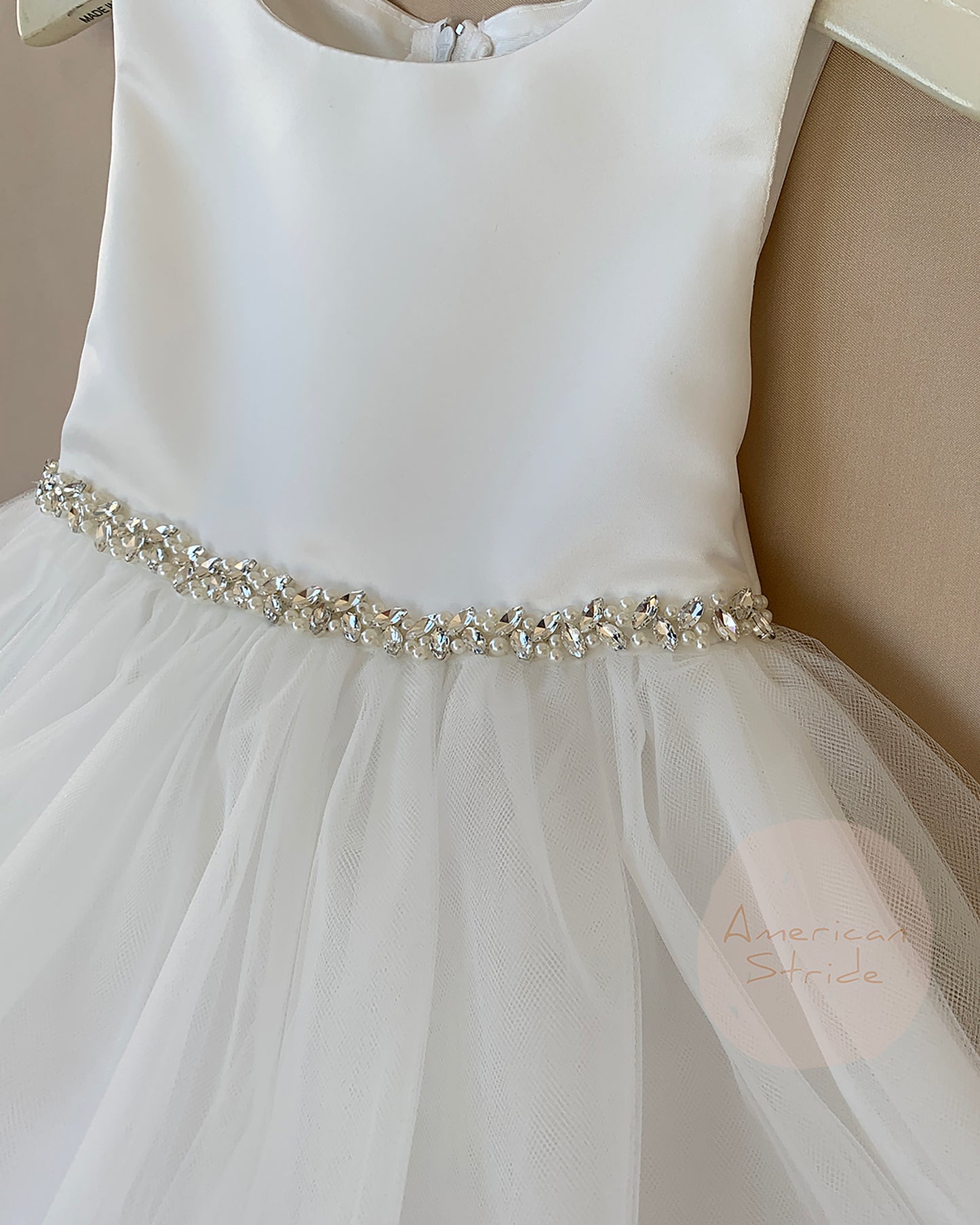 White dress with a decorative rhinestone pearl belt on a neutral background