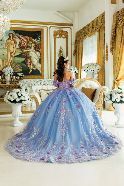 Woman standing back-facing in lilac quinceañera ball gown with off-shoulder floral appliqué sleeves, lace-up embroidered corset bodice, 3D flower details, and flowing layered skirt with train