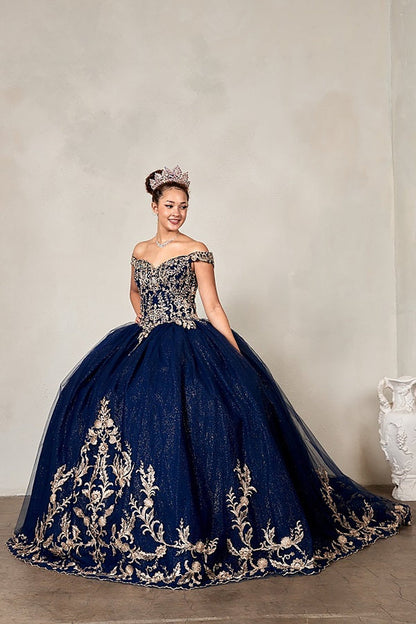 Woman in a navy blue gown with gold embroidery and a tiara against a plain background