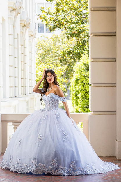 Woman in a light blue quinceañera dress standing on a balcony with greenery in the background