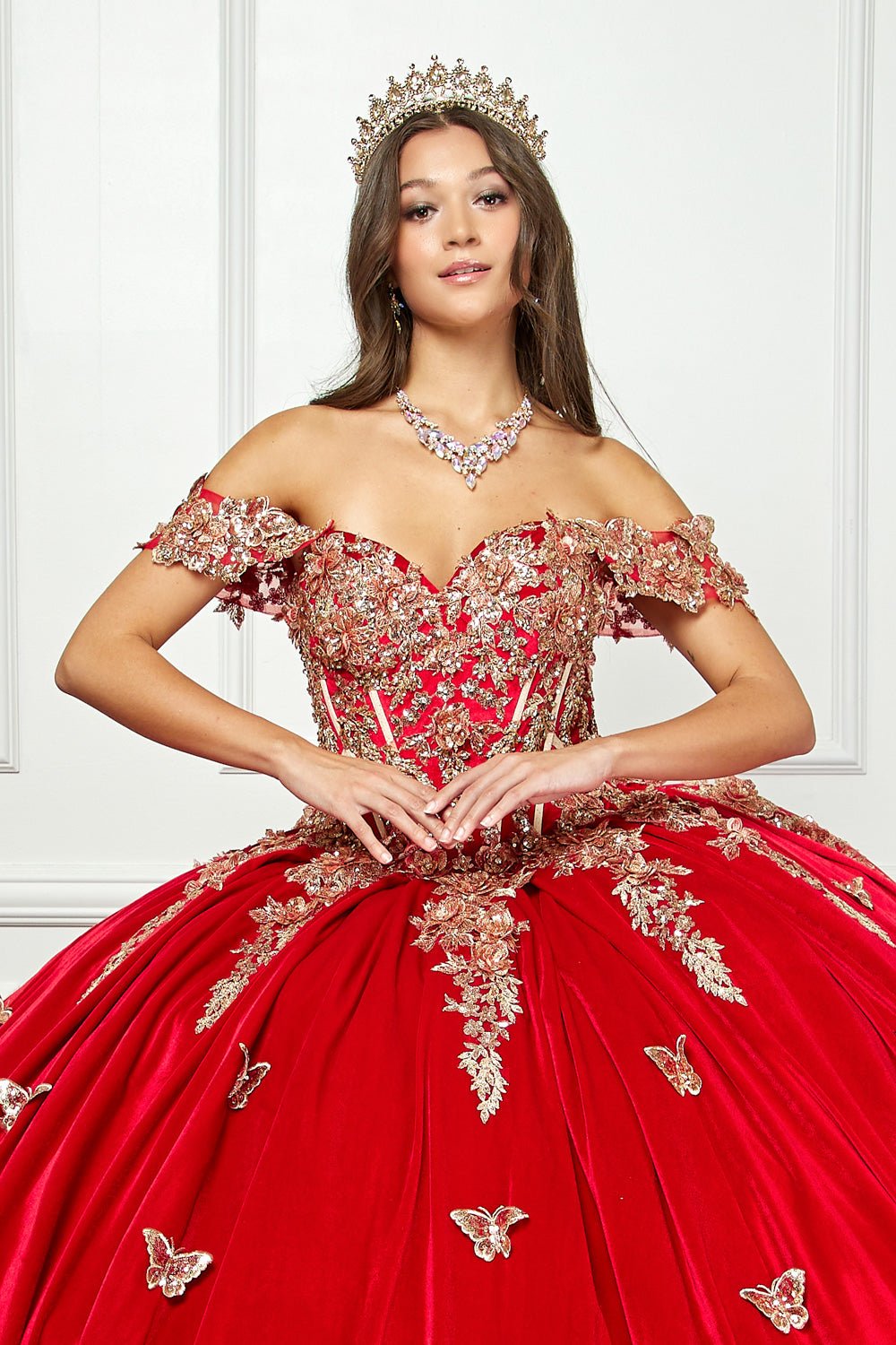 Zoomed in front view of woman wearing a red quince dress and crown. showing Off-shoulder Velvet Sweetheart Gold Sequin sequin butterfly floral on top of the dress.