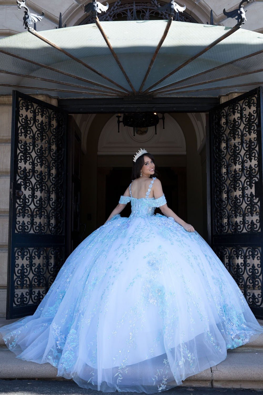 Woman in a light blue gown standing in front of an ornate building entrance.