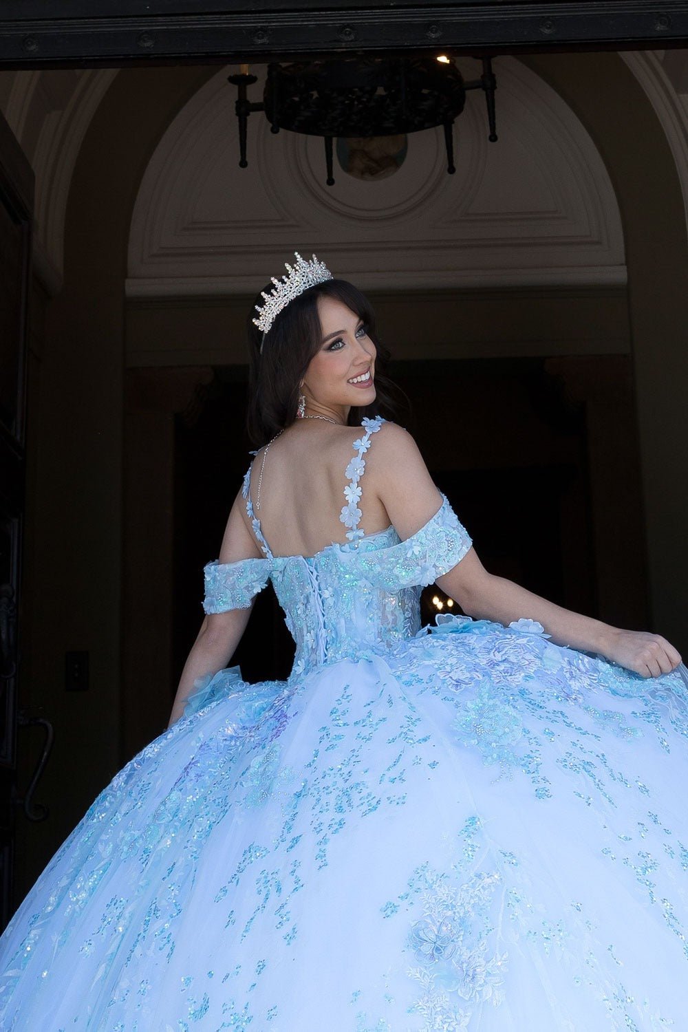 Woman in a light blue ball gown with a tiara, standing indoors.