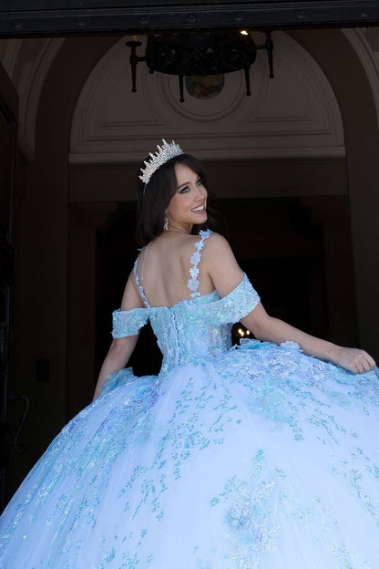 Woman in a light blue ball gown with a tiara, standing indoors.