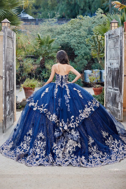 Woman in a blue quince ball gown with floral details standing in a garden setting.