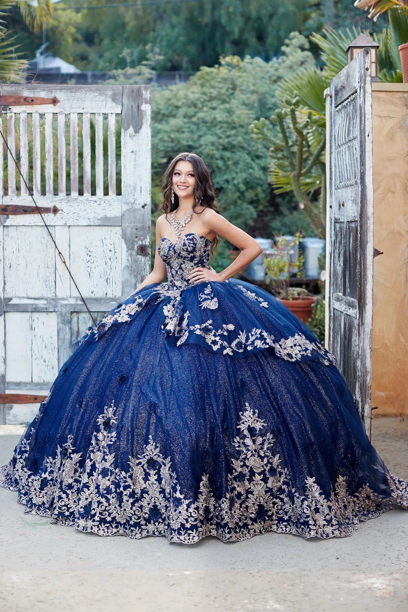 Woman in a blue and silver formal gown standing outdoors near a wooden gate.