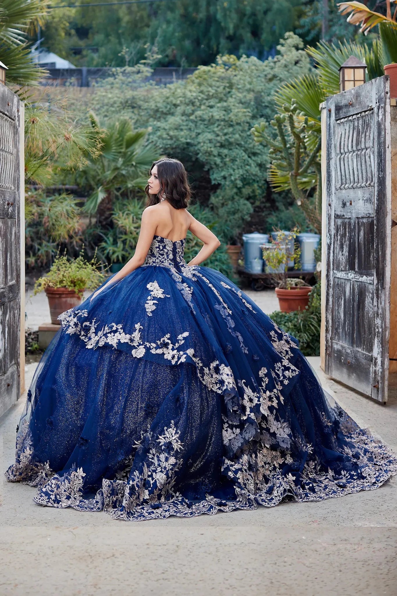 Woman in a blue floral gown standing outdoors with greenery in the background