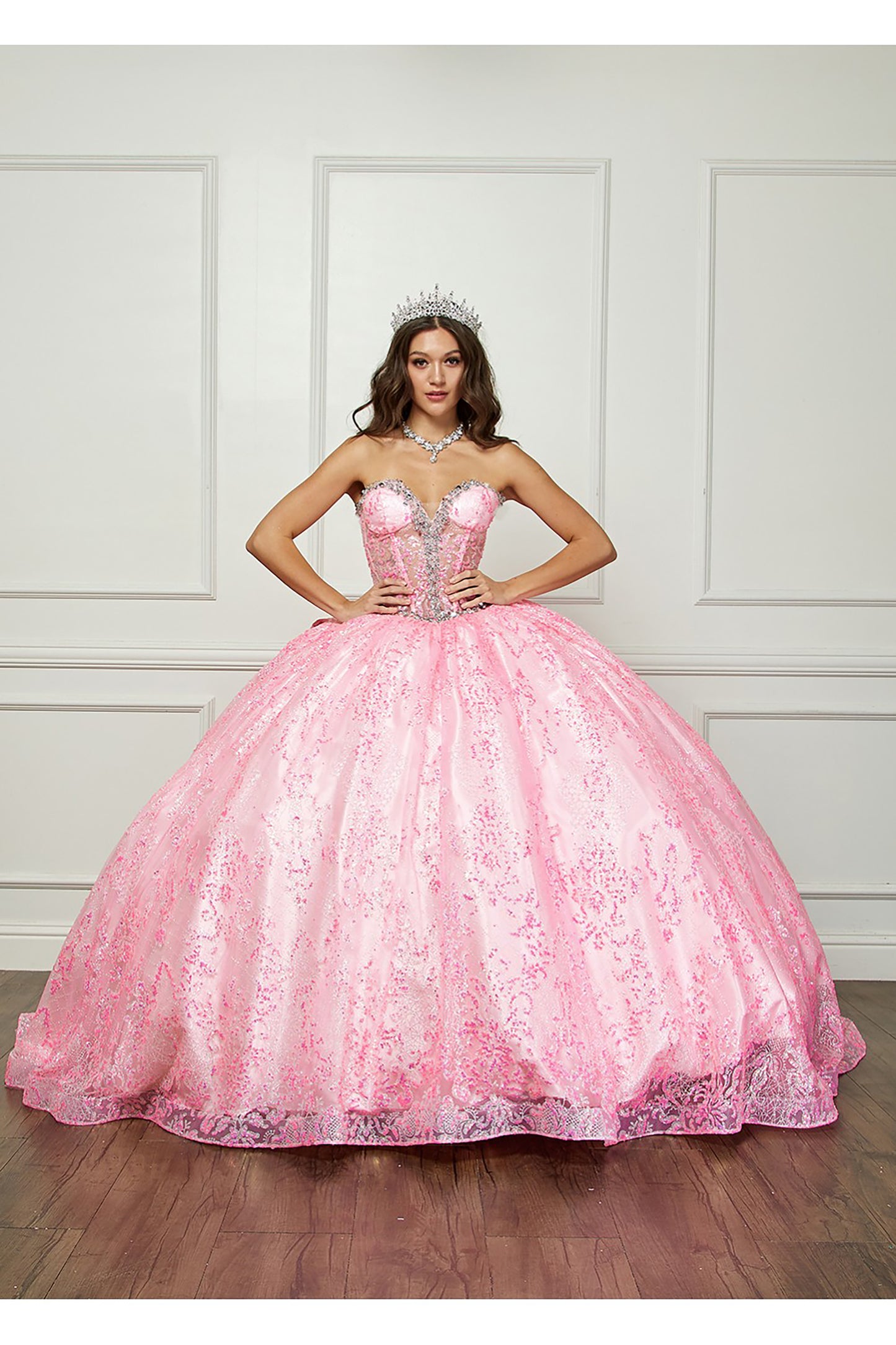 Pink Quinceanera | Spackly Sequins and Embellishments See-through Corset Bodice adorned with Shimmering Gems Quince Ballgown - front view of woman wearing dress and crown with hands on hips