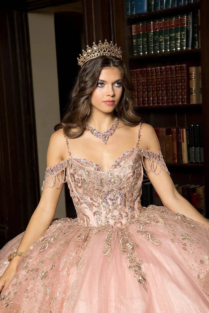 Woman in an ornate rose gold dress with a tiara and jewelry, standing in front of a bookshelf.