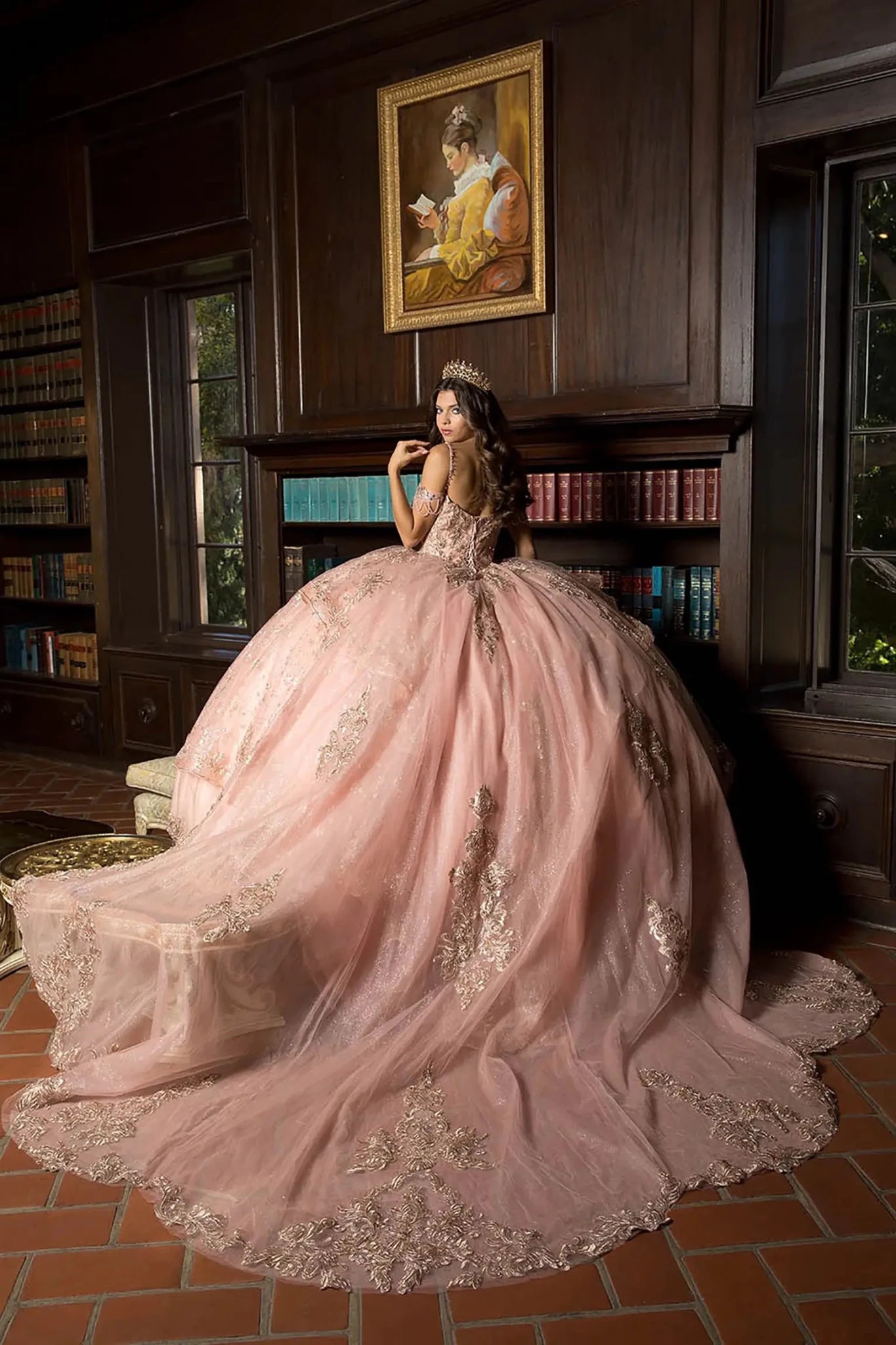 A girl in a rose gold quinceanera ball gown standing in a room with wooden paneling and bookshelves.