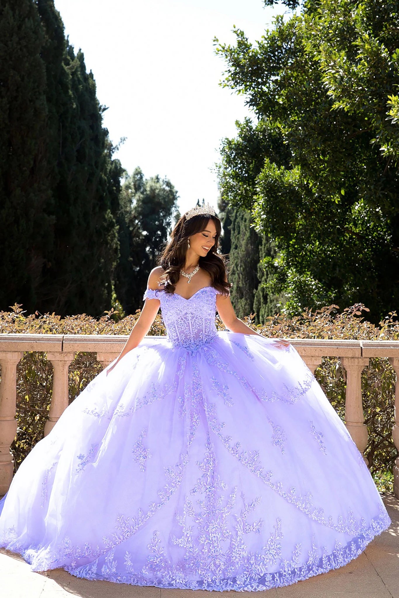 girl in a lilac quinceanera ball gown dress standing outdoors with greenery in the background