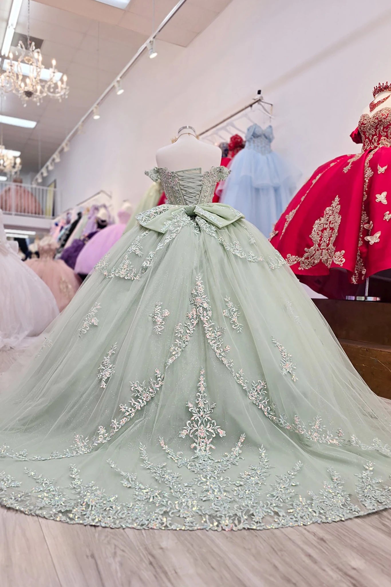 sage green evening gown with floral embellishments on a mannequin in a store setting.
