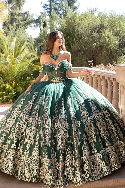 Woman in a green and gold ball gown standing outdoors with trees in the background