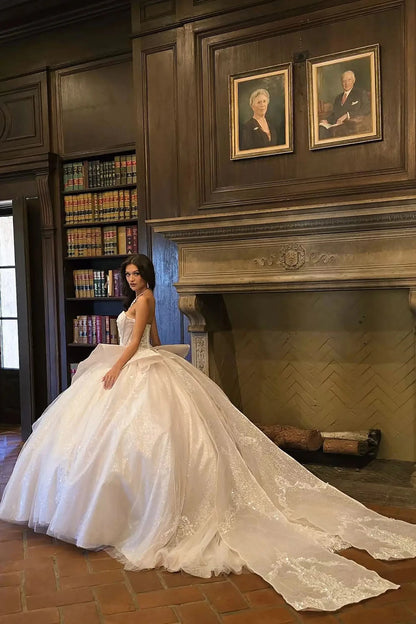 Woman in a white wedding dress sitting in front of a fireplace with portraits on the wall.