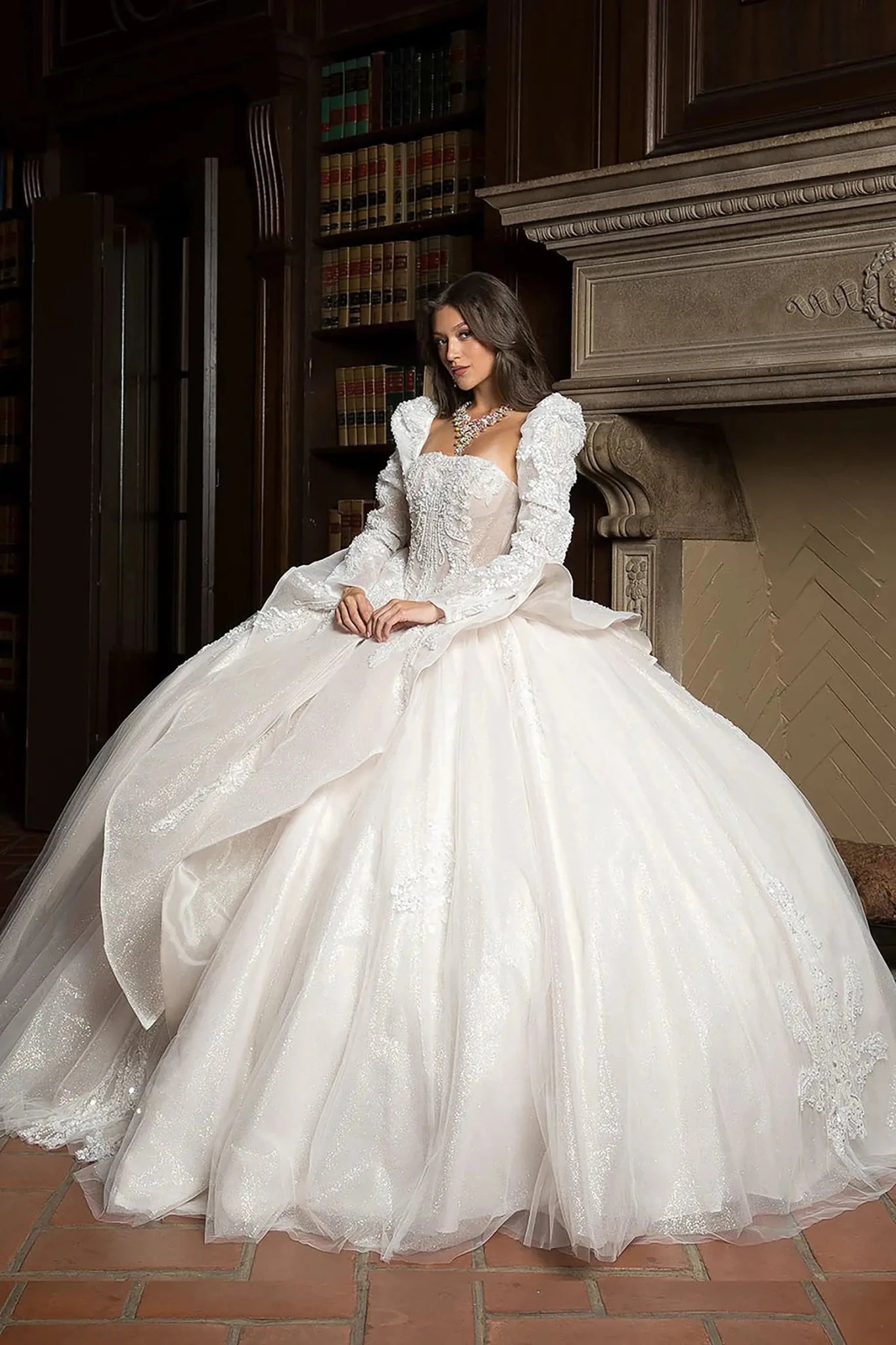 Woman in a white wedding dress sitting in a room with bookshelves and a fireplace.