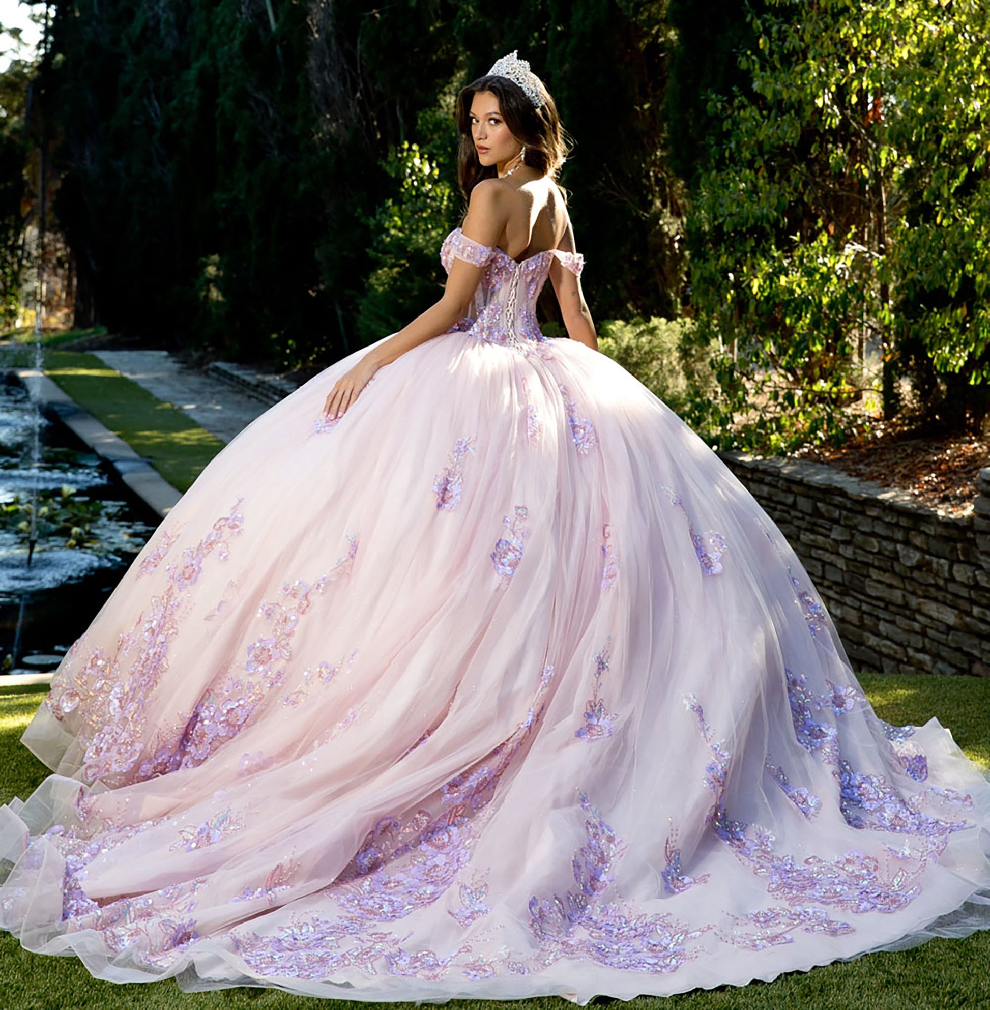 A girl wearing a blush pink quinceañera dress with floral sequins and showing her lace up back of the dress