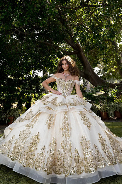 Woman wearing off-shoulder ball gown with sweetheart corset bodice, gold embroidery, layered tulle skirt, and lace-up back in an outdoor garden setting.