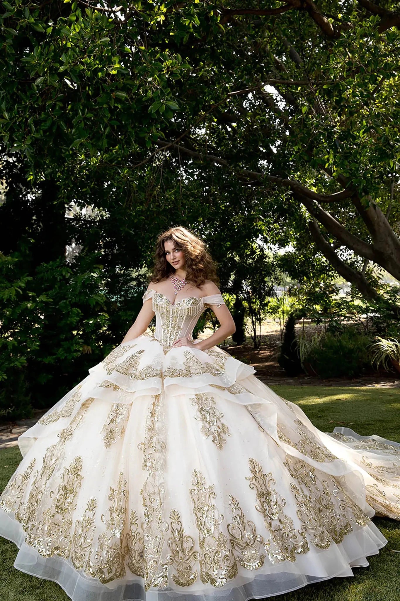 Model wearing champagne ball gown with gold beaded corset and voluminous layered tulle skirt outside.