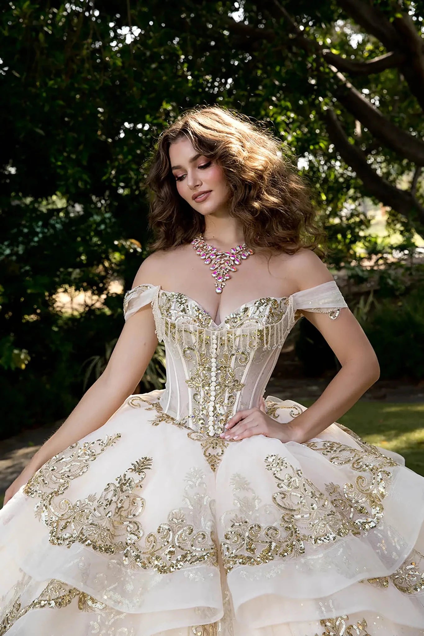 Close up model in ivory glitter tulle ball gown with lace-up corset and gold embroidery in outdoor garden.
