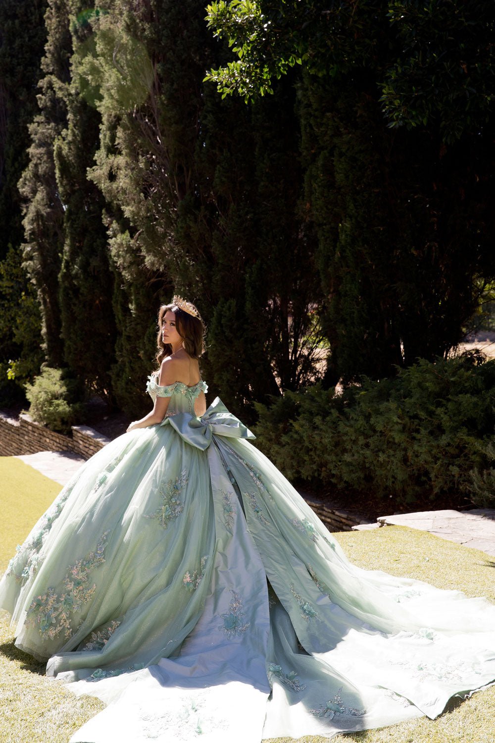 a girl in a sage quince ball gown with long satin back bow ribbon standing outdoor
