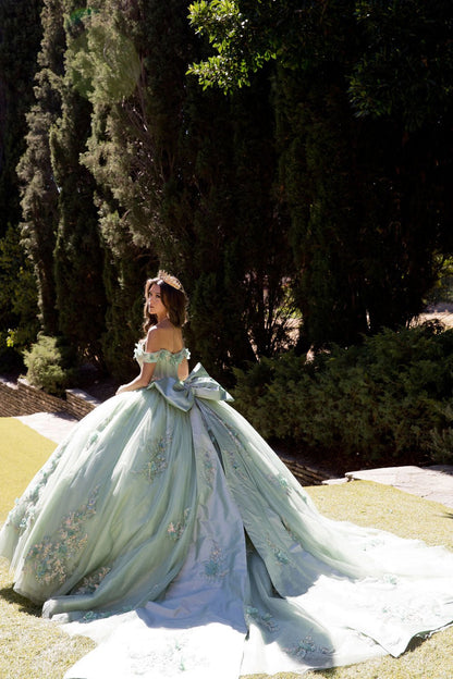 a girl in a sage quince ball gown with long satin back bow ribbon standing outdoor