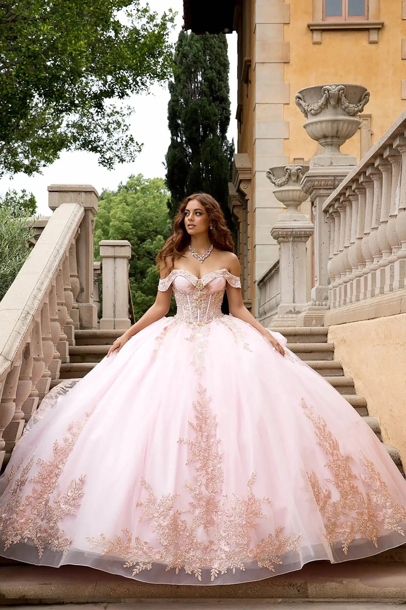 A model wearing the blush gown on an elegant stone staircase.