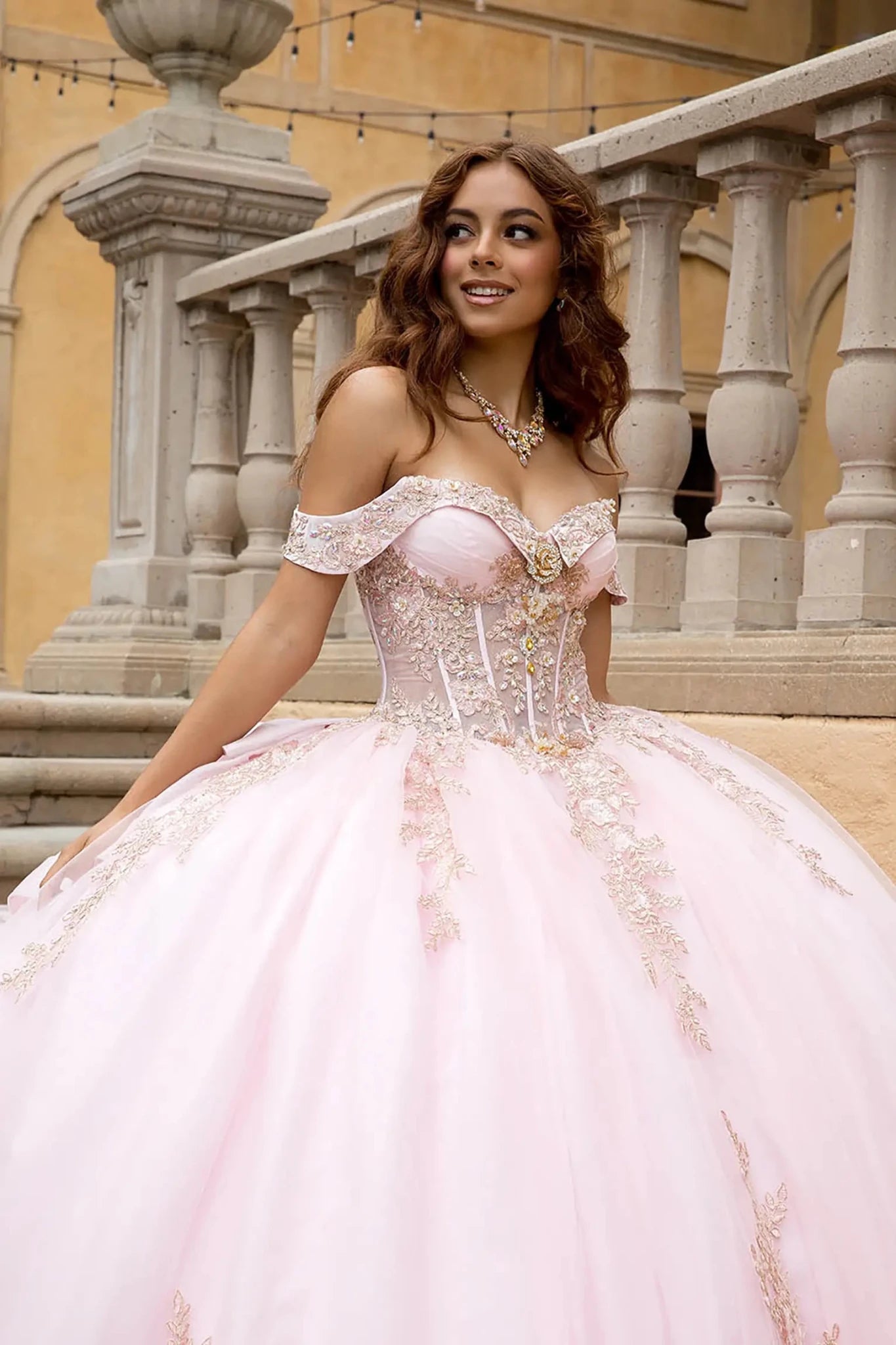 Close up blush gold sequined embroidery and the jewelry-grade beadwork on the off-the-shoulder straps. The lighting highlights the "see-through" corset panels and the subtle shimmer of the glitter tulle fabric against an elegant villa backdrop.