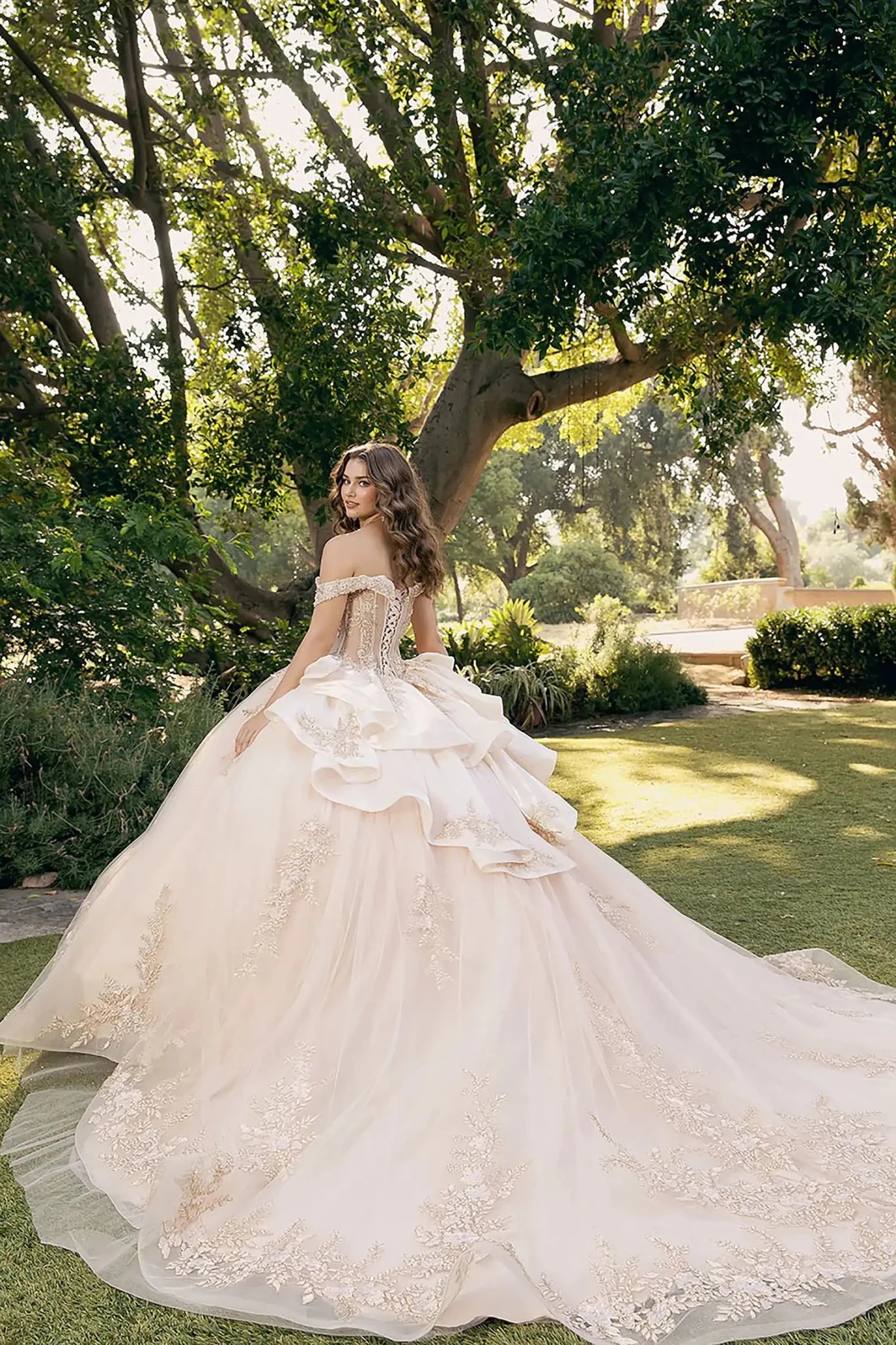 Woman standing in side profile wearing bronze ball gown with floral embellishments, crown, and voluminous skirt in elegant indoor setting