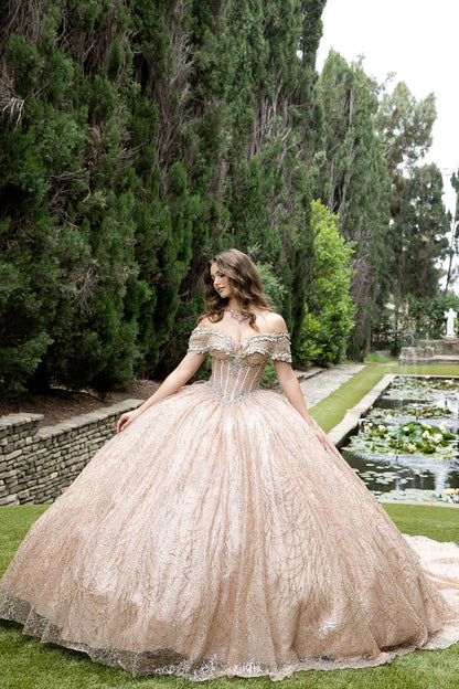 Woman in a rose gold lace dress standing outdoors with trees and water features in the background
