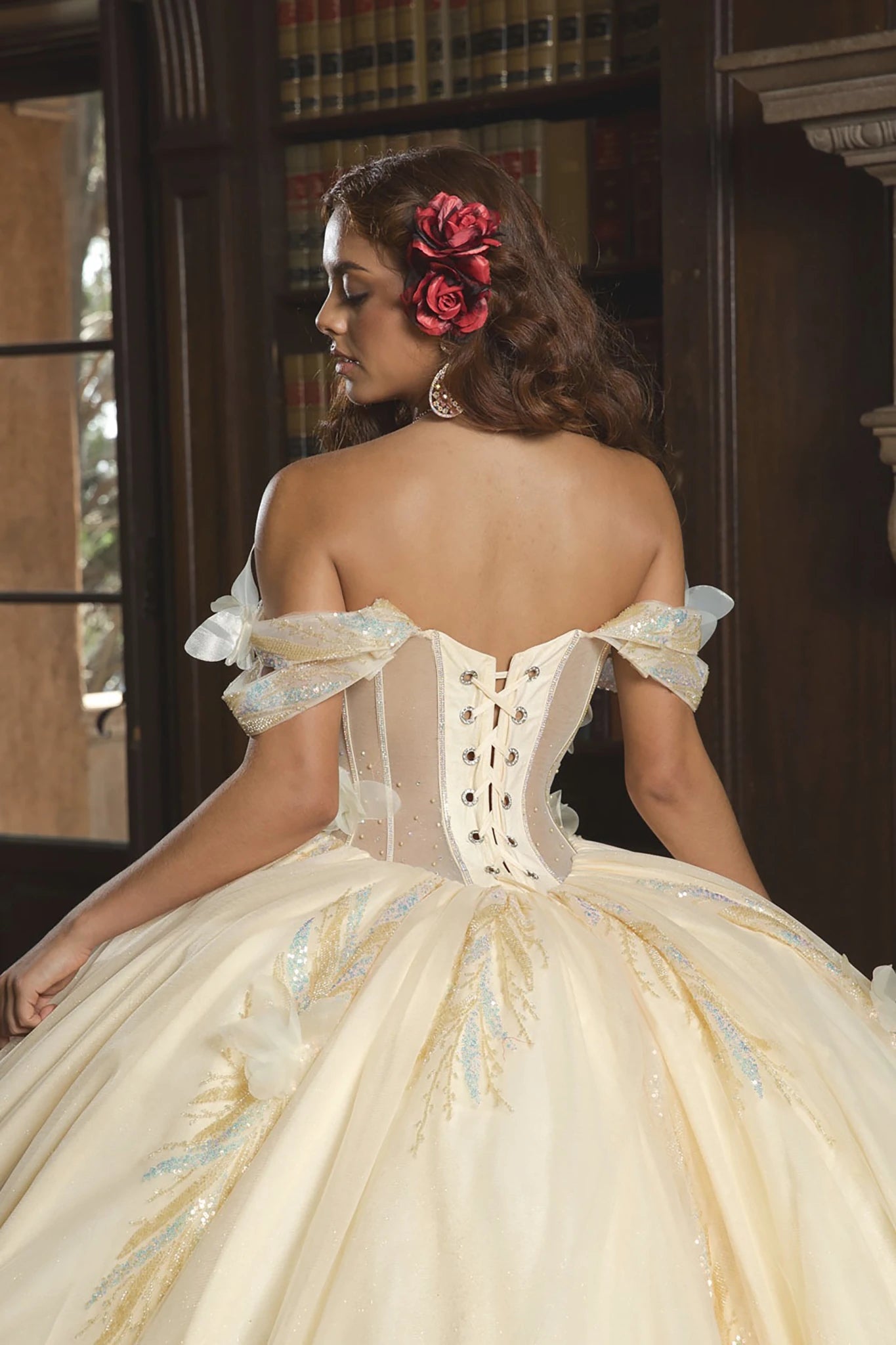 Back view of a woman wearing a beige quinceañera dress with floral details and corset bodice