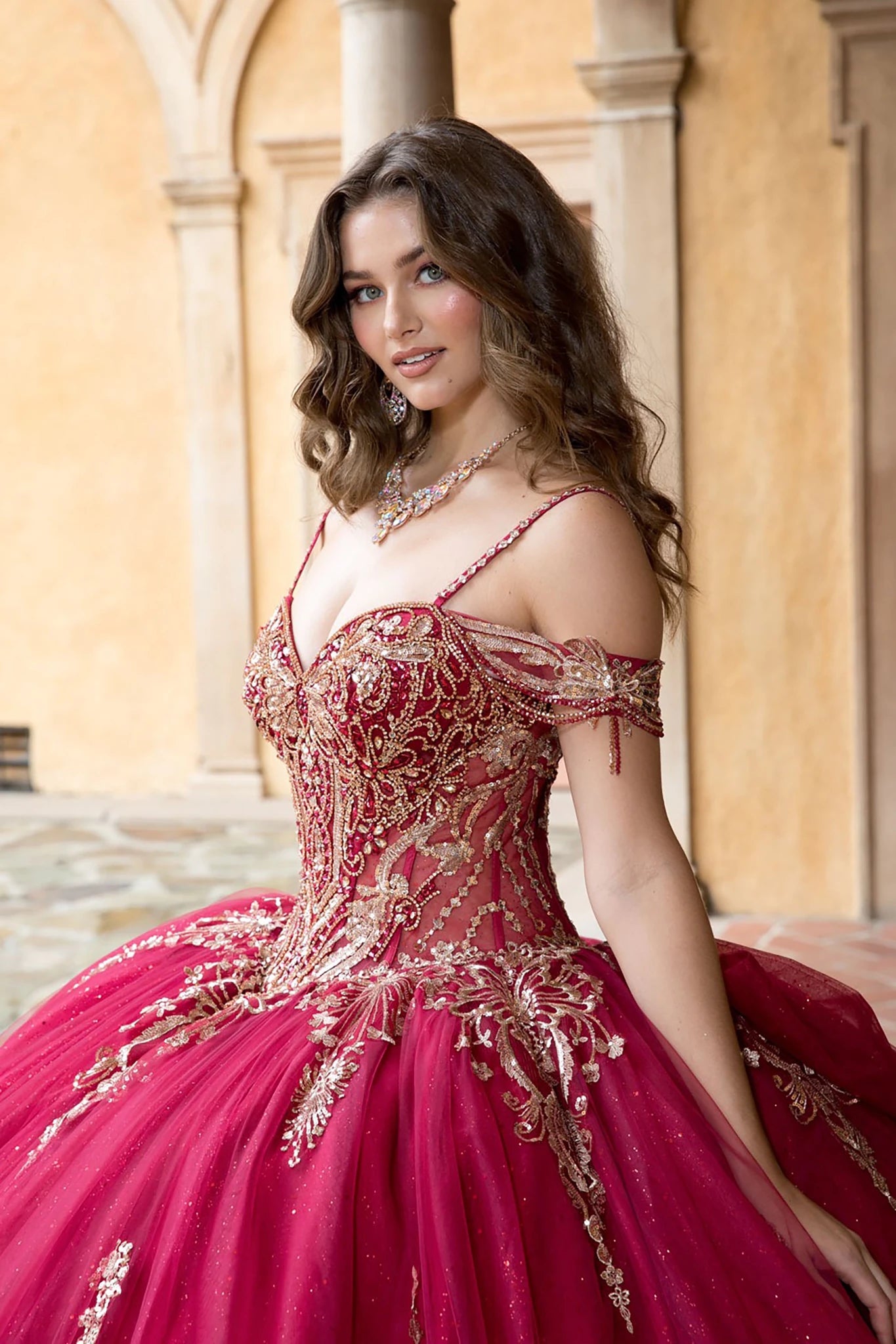 Woman in a red and gold formal gown standing in an outdoor setting with columns.