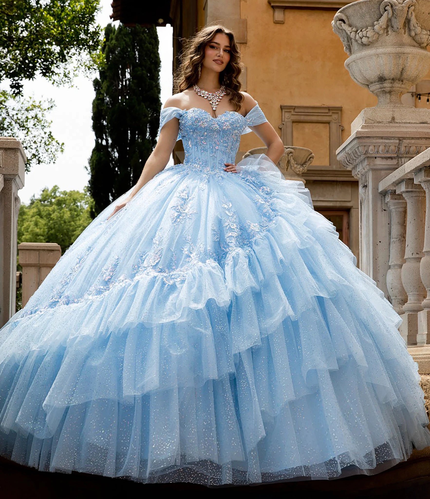Front view of a woman wearing a light blue quinceañera dress with corset bodice and layered skirt